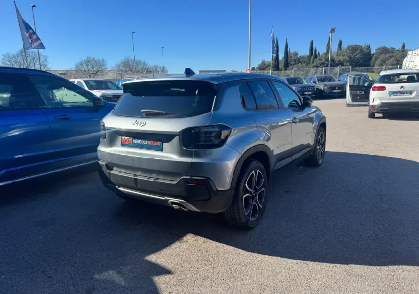 Vue 3/4 arrière droite d’un Jeep Avenger gris avec jantes alliage 18 pouces, feux arrière teintés et toit noir.