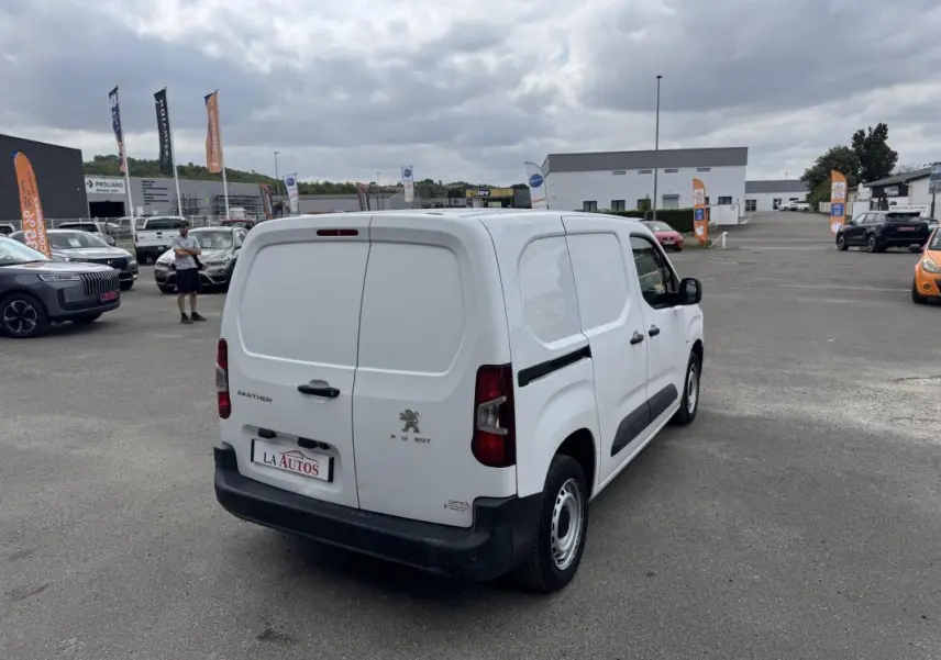Vue 3/4 arrière droite d'un Peugeot Partner blanc 2020 utilitaire avec portes arrière battantes et protections latérales noires.