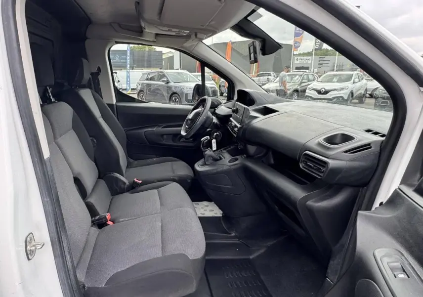 Vue intérieure côté conducteur du Peugeot Partner blanc 2020, montrant les sièges avant et le tableau de bord avec boîte manuelle.
