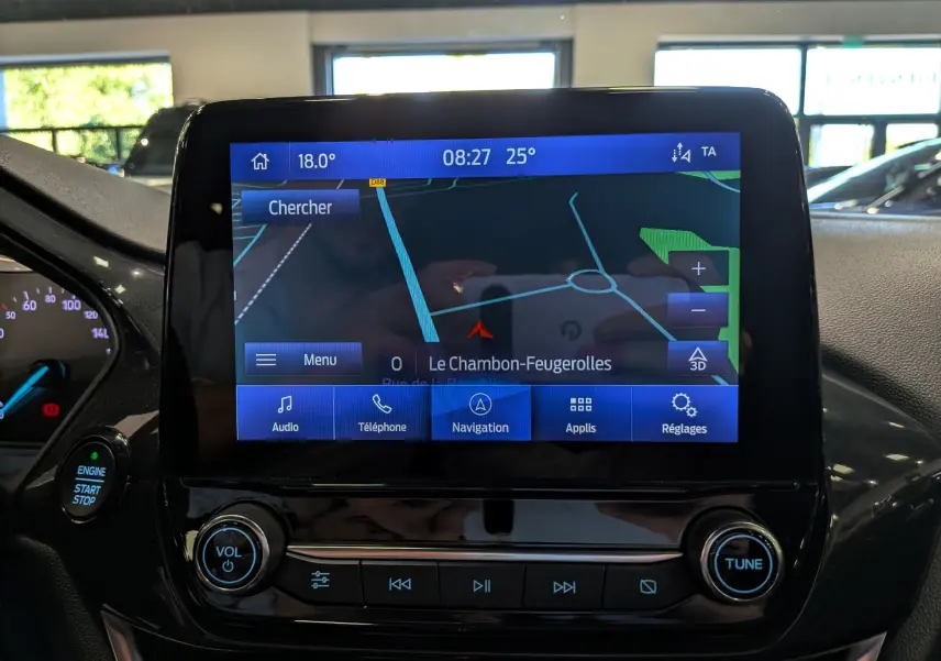 Vue rapprochée de l’écran tactile central de la Ford Fiesta blanche, affichant la navigation avec commandes audio et téléphone.