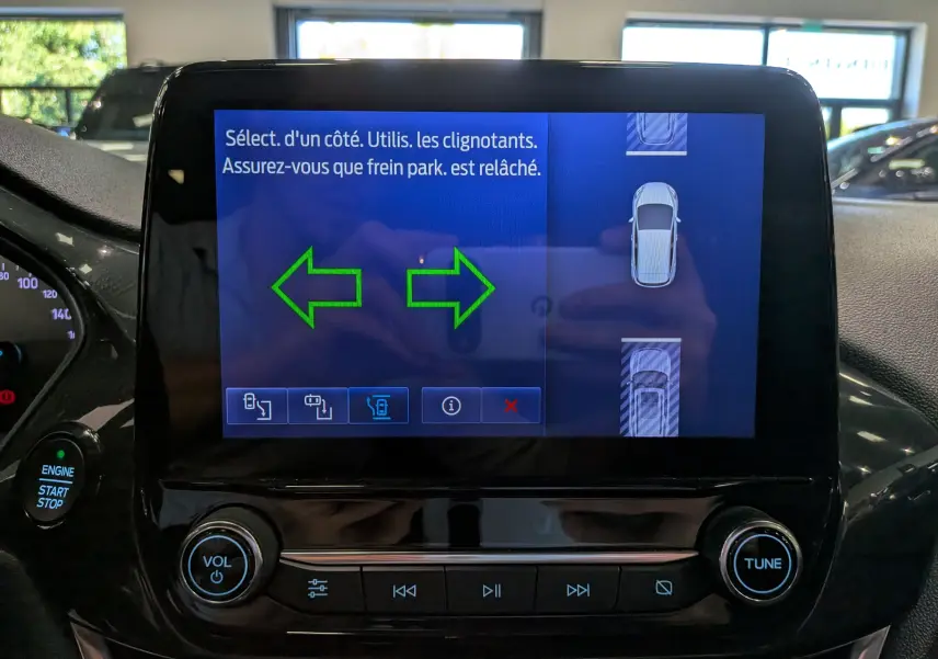 Écran tactile central de la Ford Fiesta blanche 2020 montrant l'interface d'aide au stationnement avec flèches vertes.