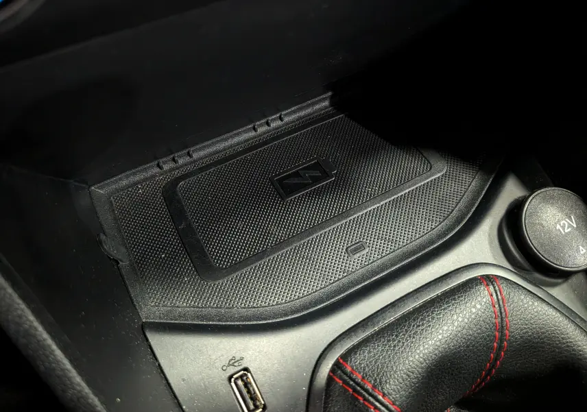 Gros plan sur la console centrale noire de la Ford Fiesta blanche, montrant le chargeur sans fil, prise USB et levier de vitesse avec surpiqûres rouges.
