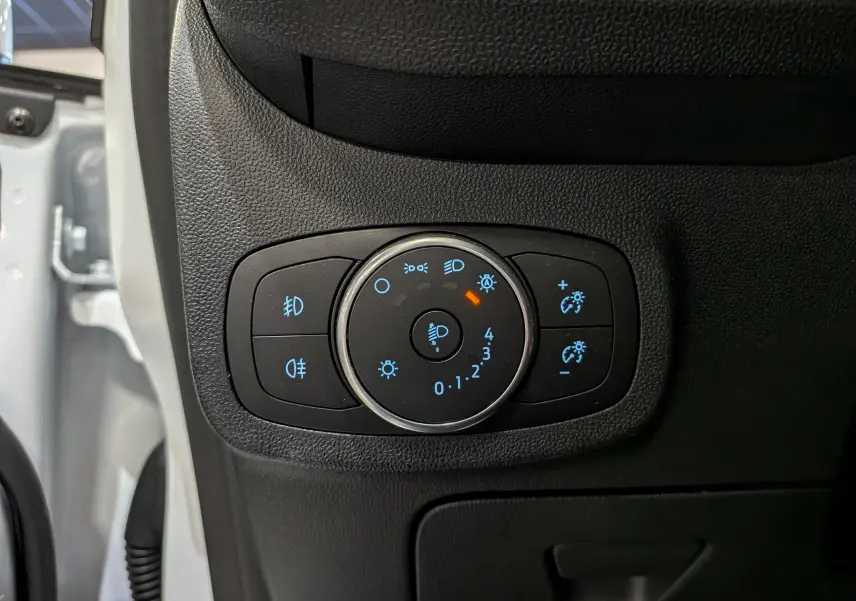 Gros plan sur le panneau de commande des phares et réglages lumineux à gauche du tableau de bord d'une Ford Fiesta blanche 2020.