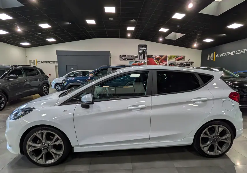 Vue de profil côté gauche d'une Ford Fiesta blanche 1.0 EcoBoost ST Line avec jantes alliage distinctives en concession.