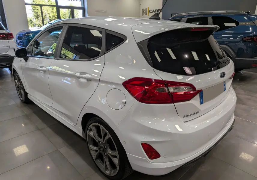 Vue 3/4 arrière droite d'une Ford Fiesta blanche 2020 en finition ST Line, avec jantes alliage et vitres teintées, en intérieur showroom.