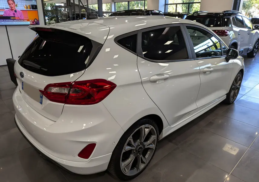 Ford Fiesta blanche 1.0 EcoBoost 95 ch ST Line vue 3/4 arrière droit en showroom avec jantes alliage.