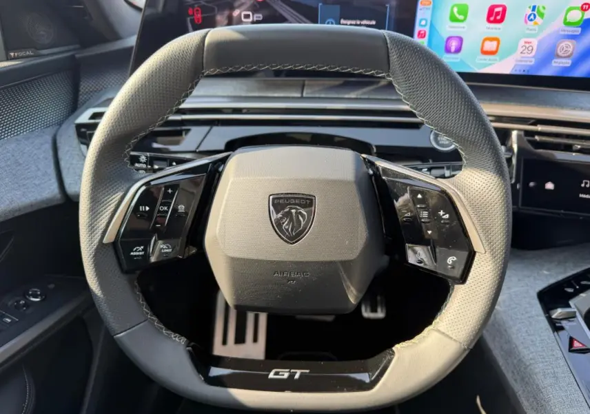 Vue rapprochée du volant gris perforé du Peugeot 3008 Hybrid 145 e-DCS6 GT avec commandes intégrées et logo central.