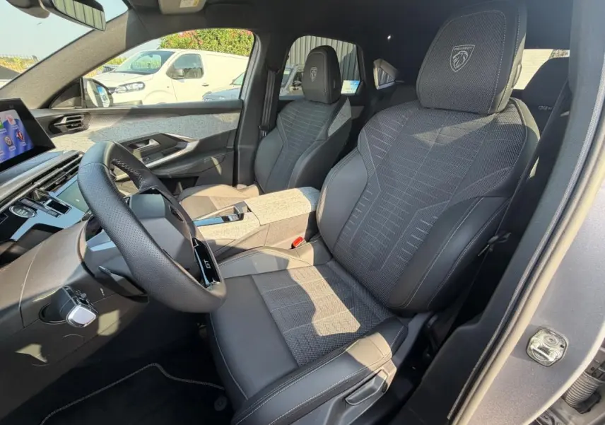 Vue intérieure côté conducteur du Peugeot 3008 Hybrid gris 2025, sièges GT avec logo Peugeot sur appuie-tête.