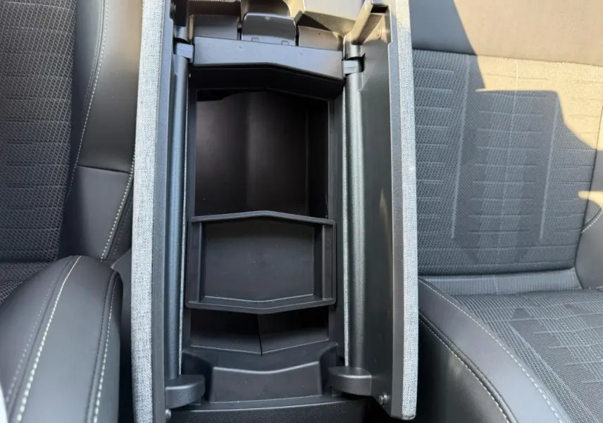 Vue plongeante sur l'accoudoir central ouvert entre les sièges tissu gris et cuir noir du Peugeot 3008 Hybrid 145 e-DCS6 GT 2025.