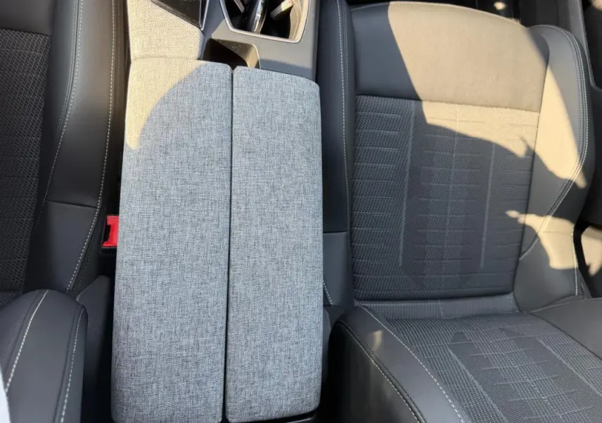 Vue rapprochée de l’accoudoir central gris et des sièges en tissu noir du Peugeot 3008 Hybrid 145 e-DCS6 GT 2025.