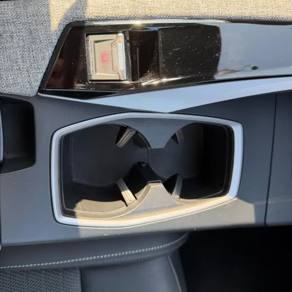 Gros plan sur la console centrale grise du Peugeot 3008 Hybrid 145 e-DCS6 GT avec porte-gobelets et frein à main électrique.