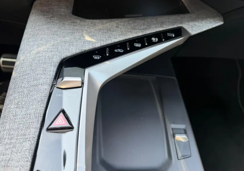 Gros plan sur la console centrale grise du Peugeot 3008 Hybrid 145 e-DCS6 GT 2025 avec boutons de commande et tissu texturé.