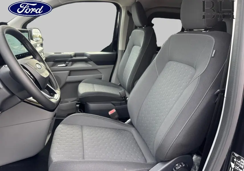 Vue intérieure côté conducteur du Ford Transit Custom Fourgon 2026, sièges tissu gris avec volant multifonction noir.