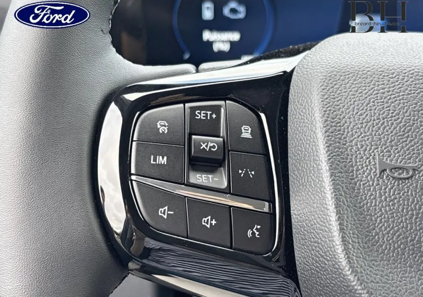 Gros plan sur les commandes multifonctions noires à gauche du volant gris du Ford Transit Custom Fourgon 2026.