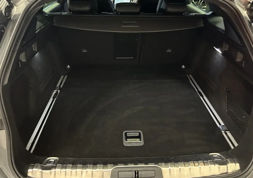 Coffre spacieux et vide de la Peugeot 508 SW 2024 gris Selenium vu de l'arrière avec banquette arrière et éclairage intérieur.