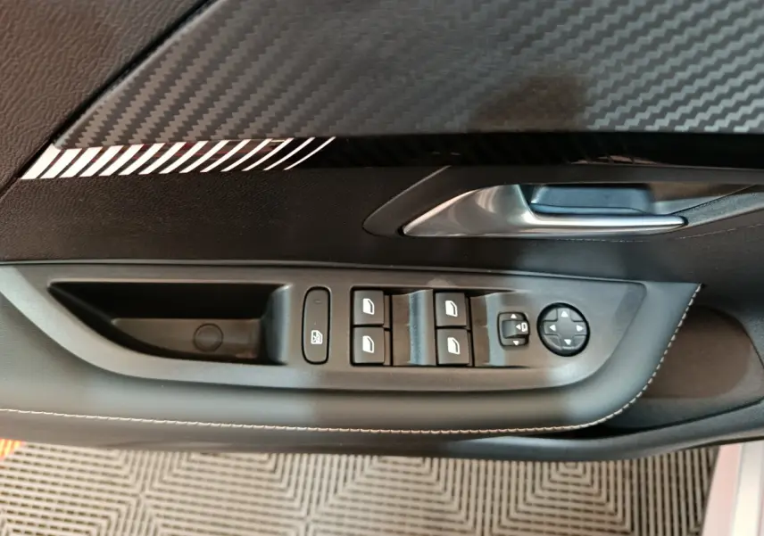 Gros plan sur la commande des vitres et rétroviseurs côté gauche intérieur de la Peugeot 208 gris clair 2025.