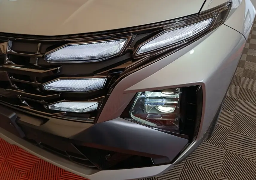 Gros plan sur l'avant droit gris clair du Hyundai Tucson 2025, mettant en valeur ses phares LED et sa calandre noire brillante.