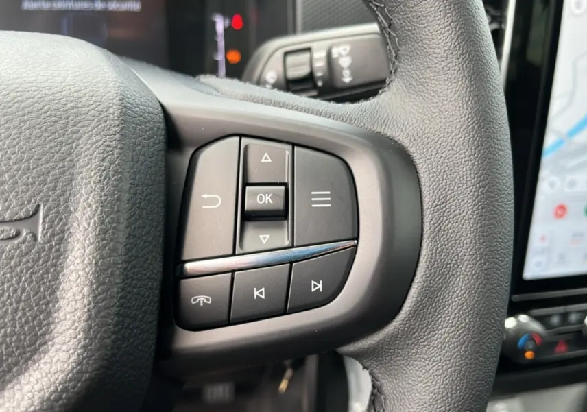 Gros plan sur les commandes multifonctions du volant cuir noir du Ford Ranger 2025 avec écran tactile en arrière-plan.