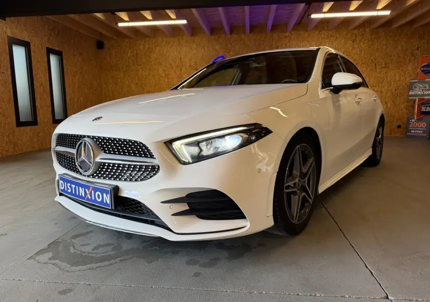 Vue 3/4 avant droite d'une Mercedes Classe A 220D AMG Line blanche avec calandre diamant et jantes AMG foncées.