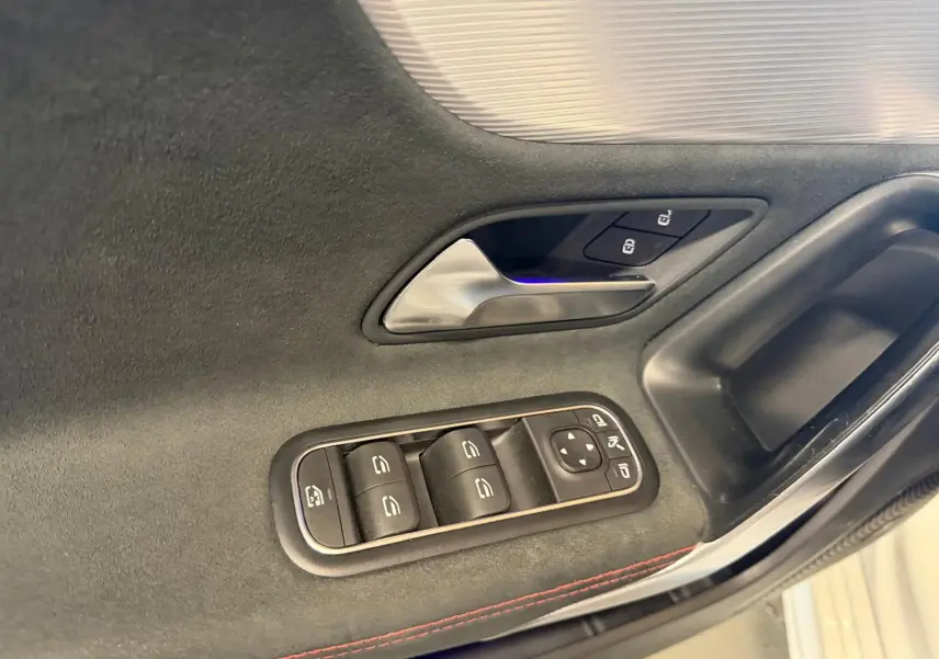 Détail de la porte côté gauche d’une Mercedes Classe A 220D AMG Line blanche, avec commandes de vitres et poignée intérieure.