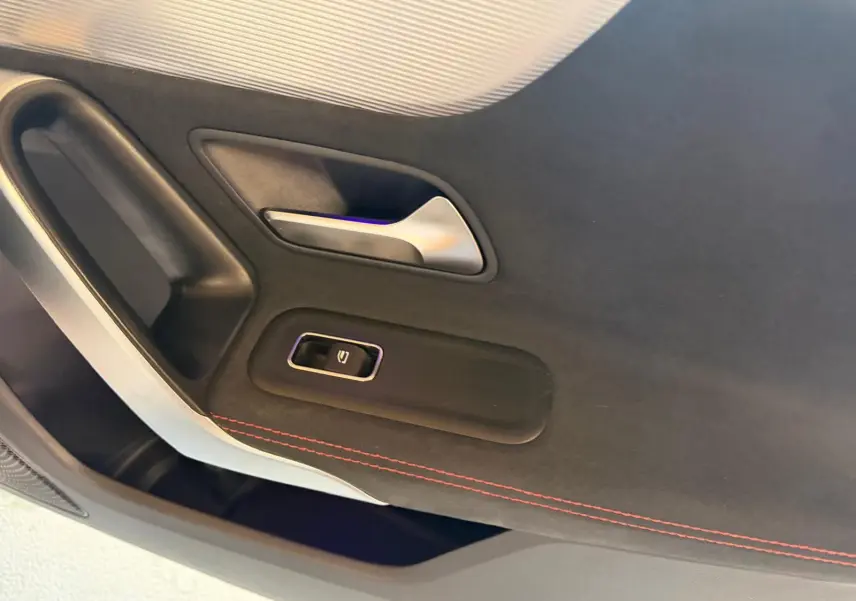 Détail de la porte intérieure côté gauche de la Mercedes Classe A 220D AMG Line blanche avec couture rouge et bouton de lève-vitre.