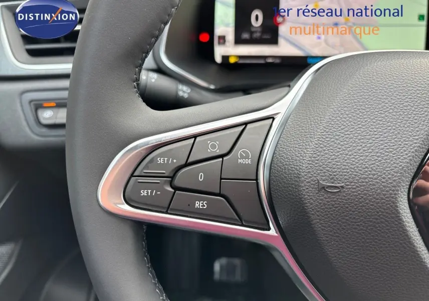 Gros plan sur les commandes à gauche du volant gris cuir du Renault Captur II hybride, tableau de bord numérique en arrière-plan.