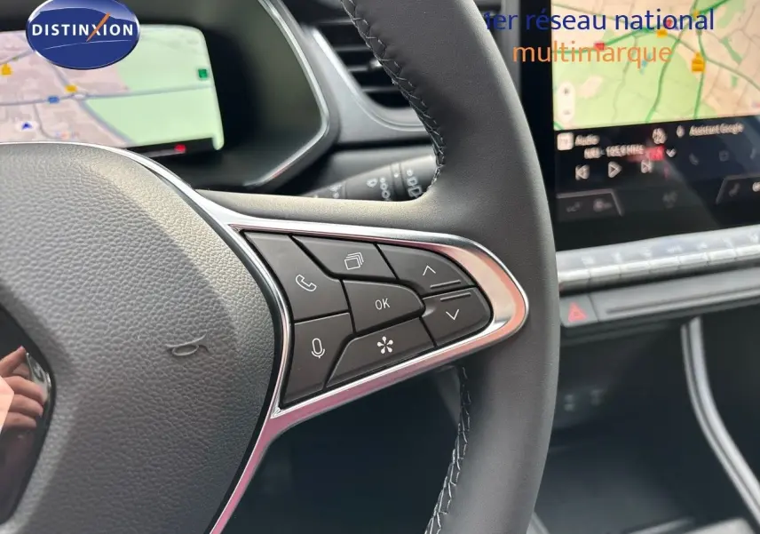 Gros plan sur le volant cuir noir du Renault Captur 2025, avec commandes multifonctions et écran tactile de navigation en arrière-plan.