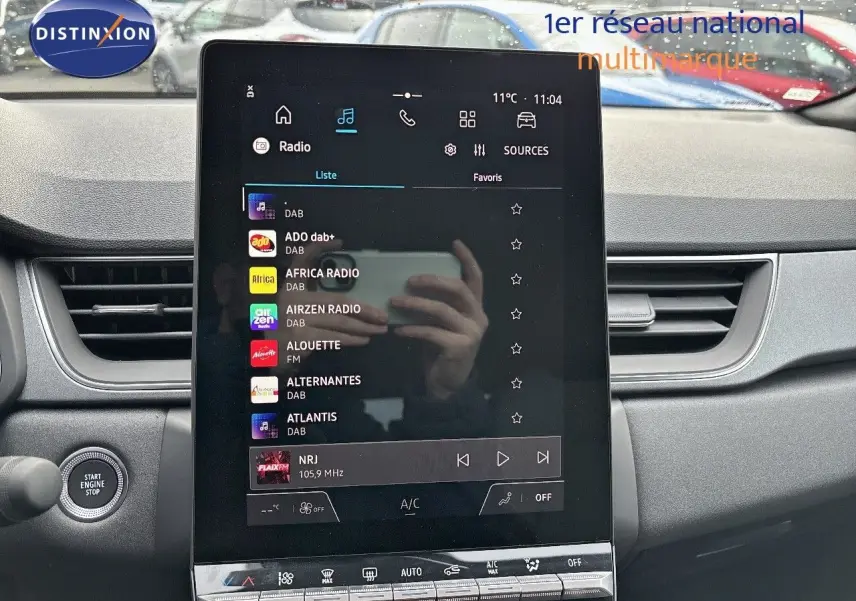 Vue rapprochée de l’écran tactile central du Renault Captur II hybride 2025, affichant les stations radio, avec tableau de bord gris.