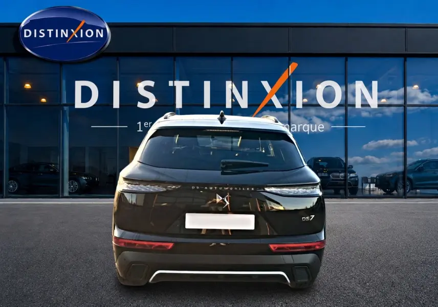 Vue arrière d'un DS7 noir 2026 stationné devant une vitrine avec logo Distinxion visible en reflet.