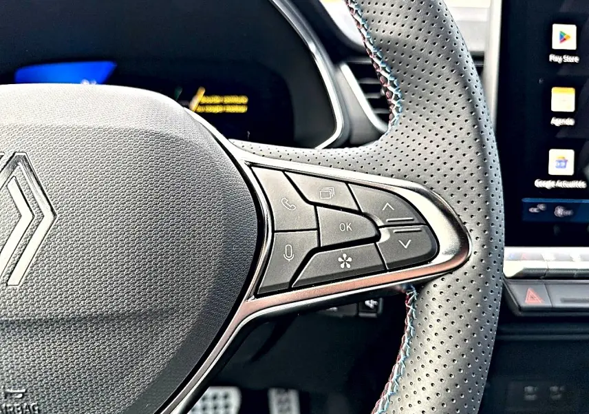 Gros plan sur le volant perforé avec commandes multifonctions du Renault Symbioz gris rafale, tableau de bord et écran tactile visibles.