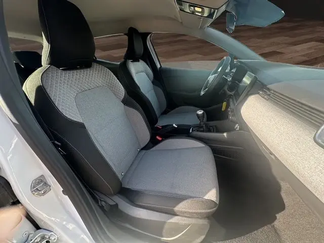 Intérieur avant droit d'une Renault Clio V blanche 2025, sièges tissu gris à motif 3D et tableau de bord clair.