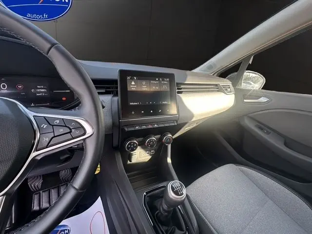 Intérieur avant droit de la Renault Clio V blanche, volant textile, écran tactile Easy Link 7'' et levier de vitesse manuel visible.