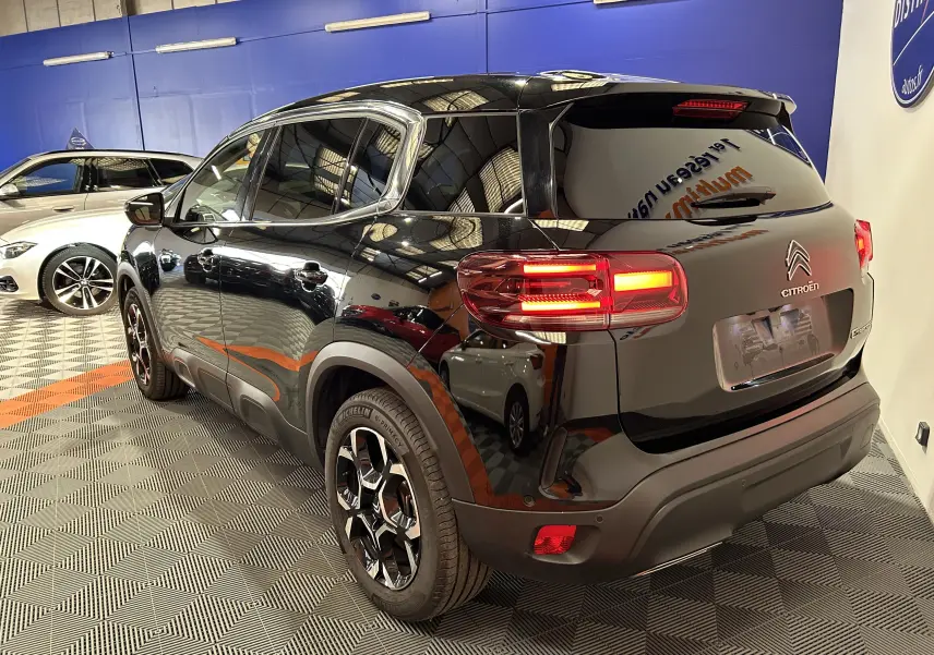 Vue 3/4 arrière droite du Citroën C5 Aircross noir Perla Nera avec feux allumés dans un showroom intérieur.