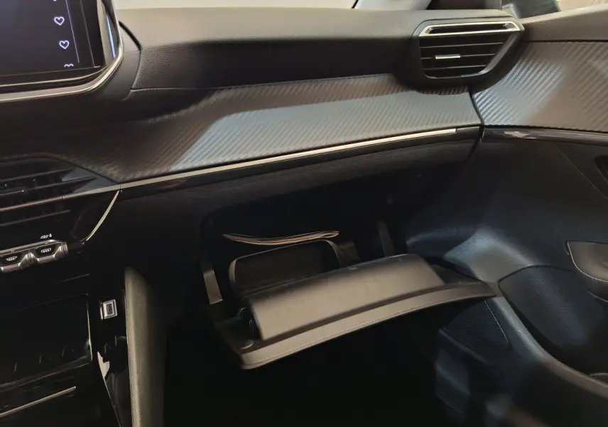 Gros plan sur la boîte à gants ouverte et le tableau de bord gris carbone intérieur de la Peugeot 208 PureTech 100 S&S Allure 2025