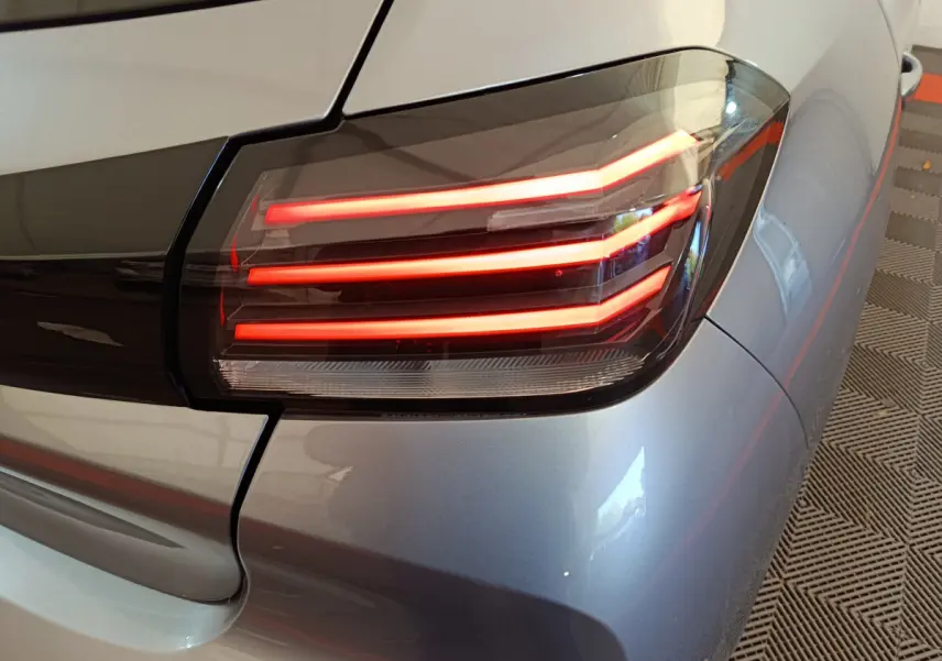 Gros plan sur le feu arrière droit rouge d'une Peugeot 208 gris clair, soulignant son design moderne et épuré.