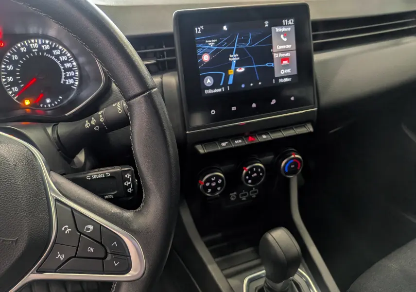 Vue intérieure de la Renault Clio V TCe 90 gris platine, avec tableau de bord, écran tactile et levier de boîte auto.