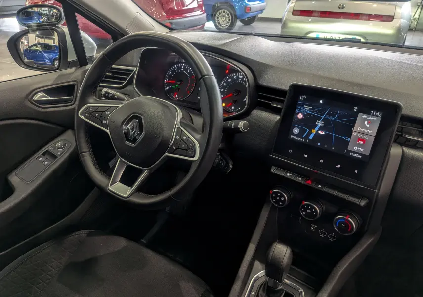Vue intérieure côté conducteur de la Renault Clio V Gris Platine, avec tableau de bord, volant et écran tactile central allumé.