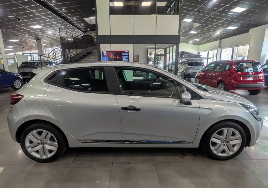 Profil côté gauche de la Renault Clio V gris platine 2021 en version TCe 90 CH X-TRONIC, dans un showroom lumineux.