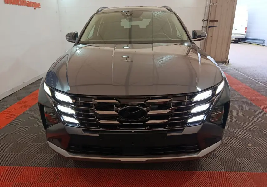 Vue avant d’un Hyundai Tucson gris foncé 2025 avec calandre chromée et feux LED allumés dans un garage.