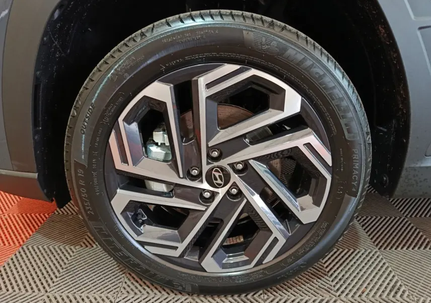 Gros plan sur la roue avant gauche du Hyundai Tucson gris foncé, mettant en valeur la jante alliage au design géométrique.