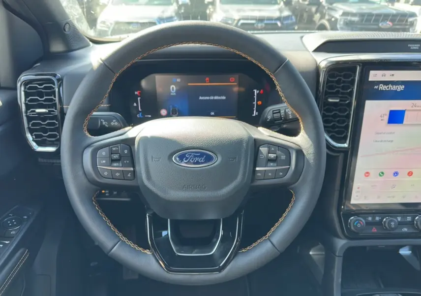 Vue rapprochée du volant cuir noir avec surpiqûres marron du Ford Ranger 2026, tableau de bord et écran tactile visibles.