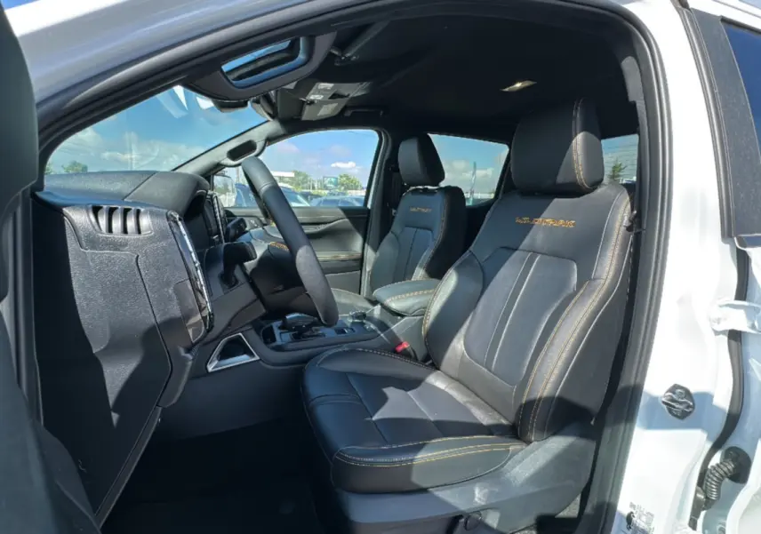 Vue intérieure côté conducteur du Ford Ranger blanc 2026, sièges cuir noirs avec surpiqûres jaunes Wildtrak visibles.