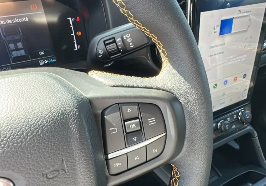 Gros plan sur le volant cuir noir avec surpiqûres jaunes du Ford Ranger 2026, écran tactile et commandes au volant visibles.