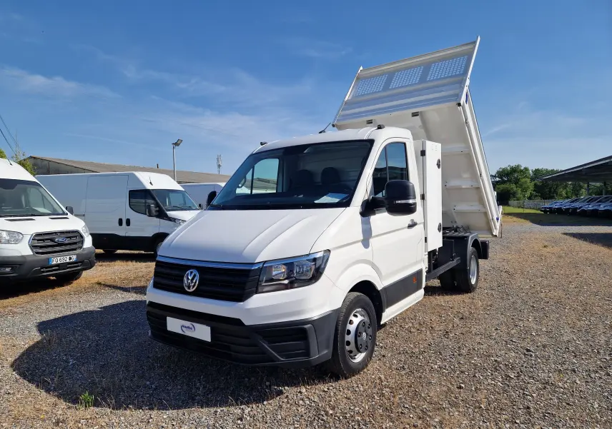 Volkswagen Crafter blanc vu 3/4 avant droit avec benne relevée et coffre latéral sur terrain gravillonné.