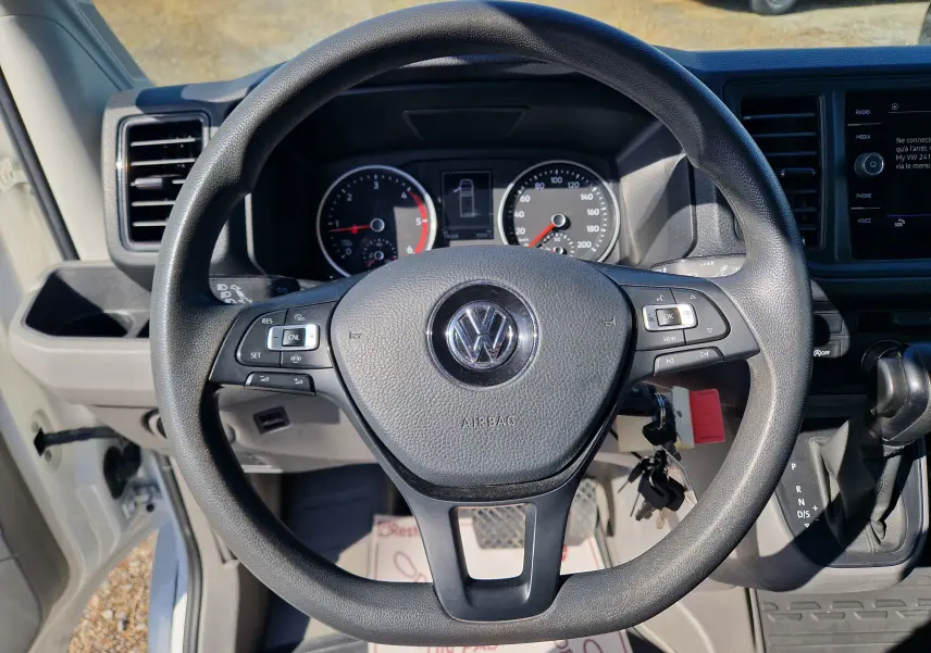 Vue intérieure centrée sur le volant noir du Volkswagen Crafter blanc, avec tableau de bord et levier de vitesses automatique visibles.
