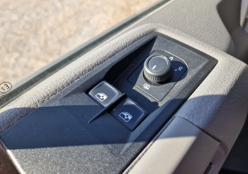 Gros plan sur les commandes de réglage des rétroviseurs et vitres électriques côté conducteur d’un Volkswagen Crafter blanc.