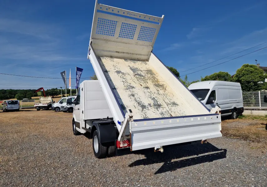 Volkswagen Crafter blanc vu de l'arrière avec benne relevée et coffre, sur un terrain extérieur ensoleillé.