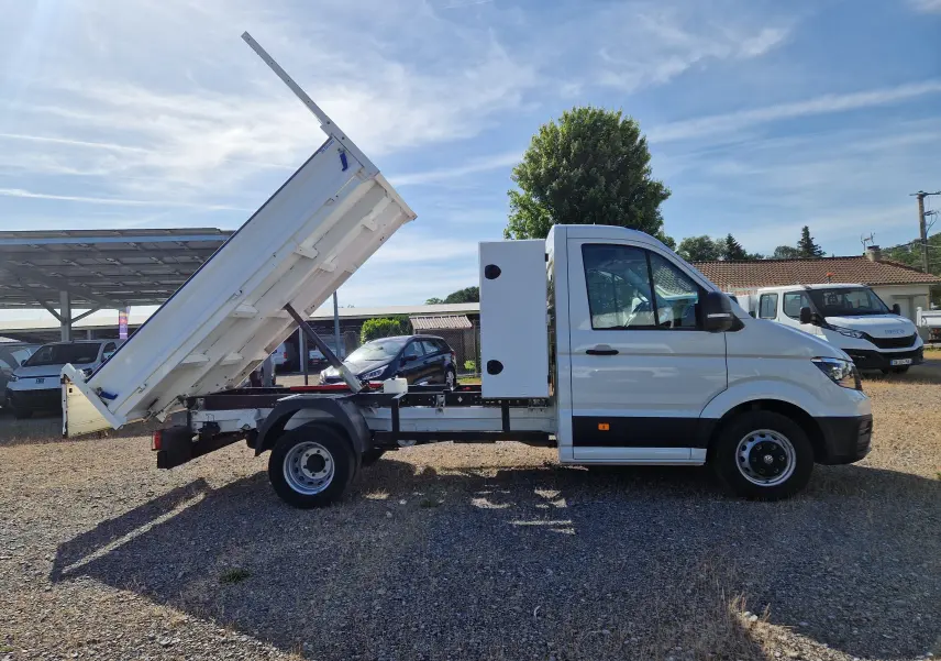 Volkswagen Crafter blanc en vue latérale droite, benne relevée avec coffre arrière et roues jumelées visibles.