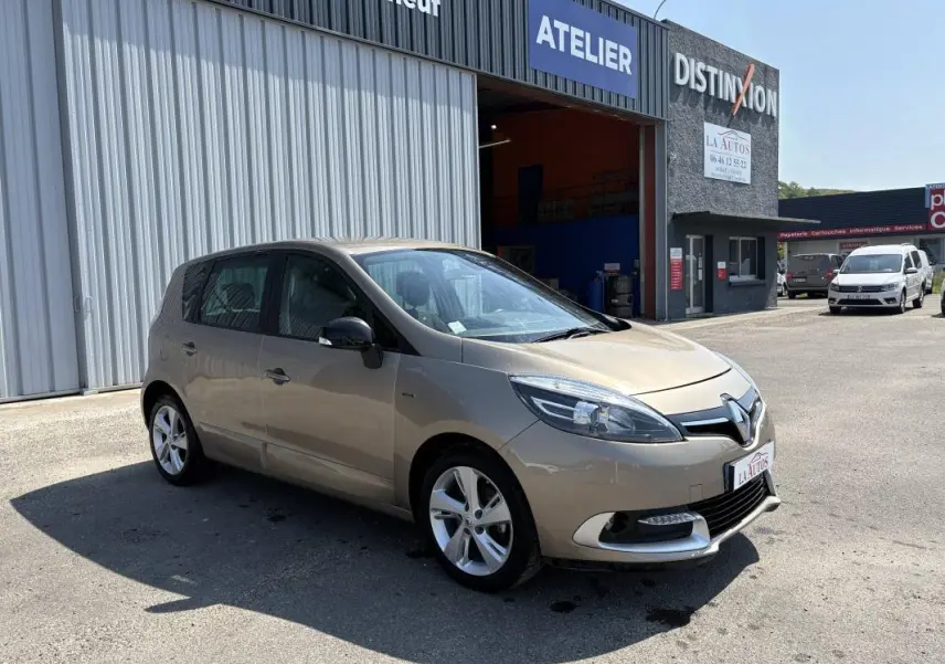 Renault Scénic III beige vue 3/4 avant droit, jantes aluminium, stationné devant un atelier automobile.