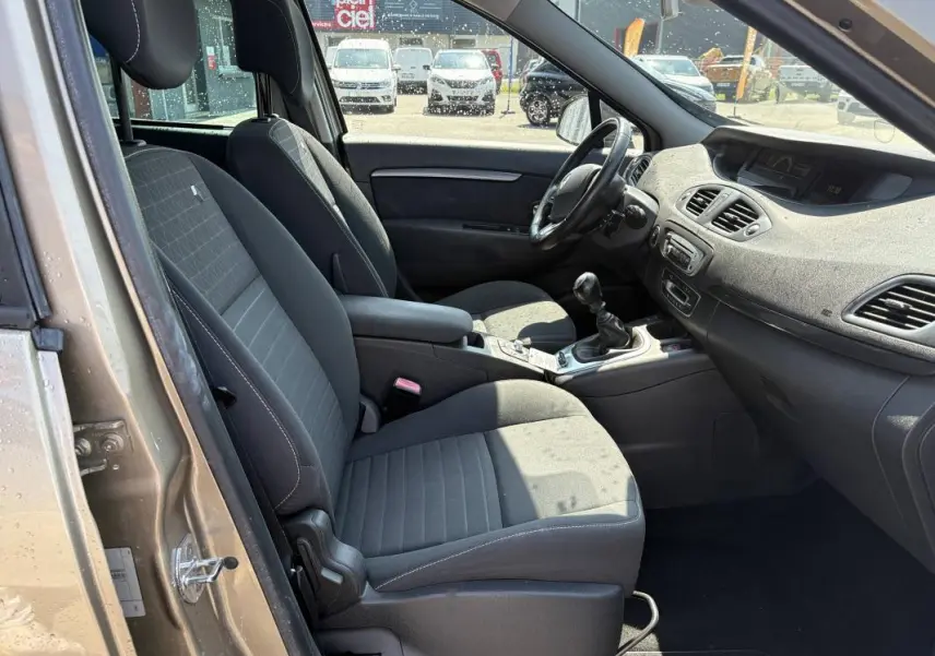 Vue intérieure côté conducteur du Renault Scénic beige, montrant sièges tissu, volant cuir et console centrale avec boîte manuelle.